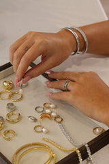 Hands arranging gold-plated and silver jewellery pieces in a display tray