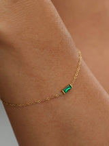 Gold birthstone bracelet with a green baguette stone worn on the wrist