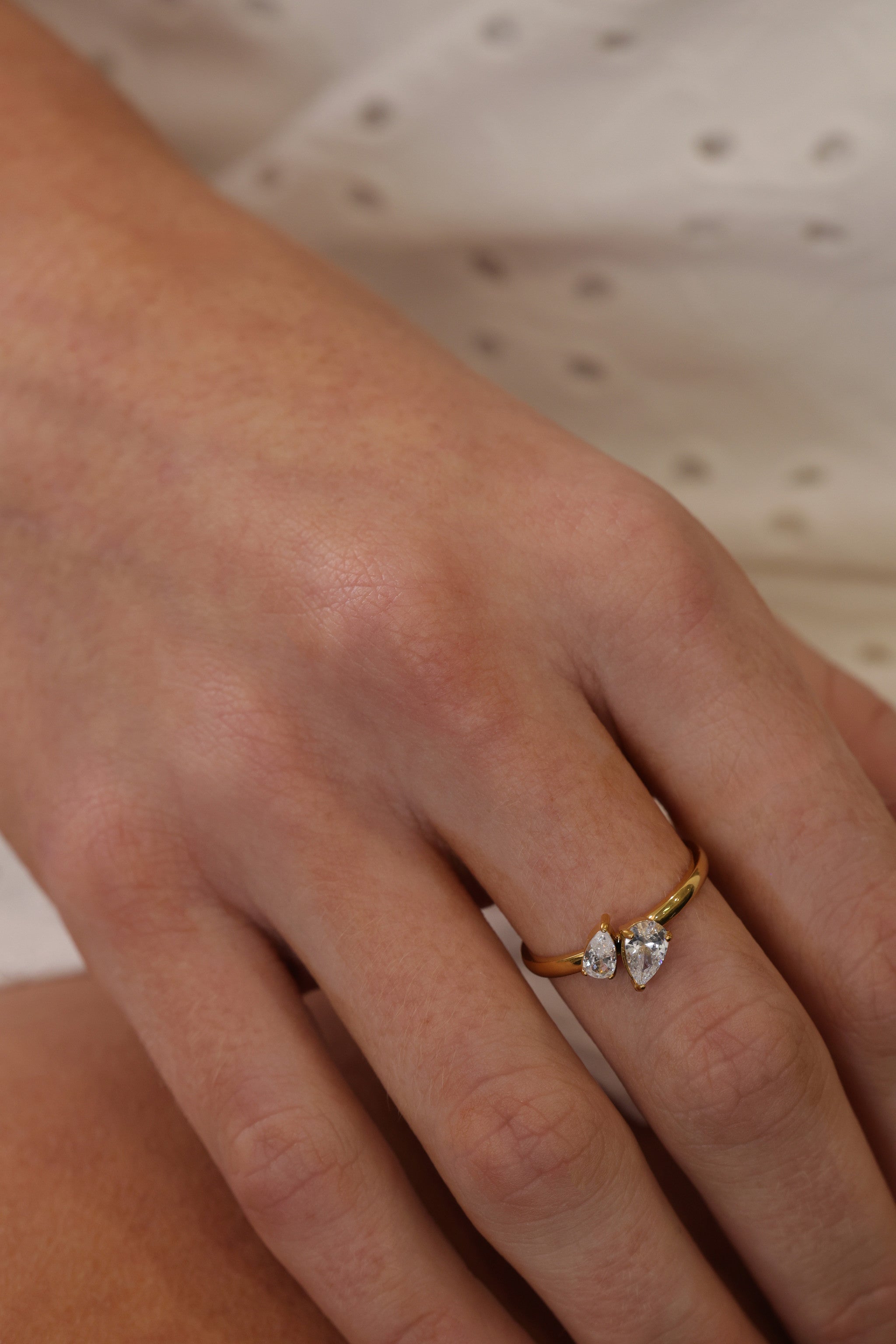 Elodie toi et moi pear ring in gold worn on a hand against white eyelet fabric