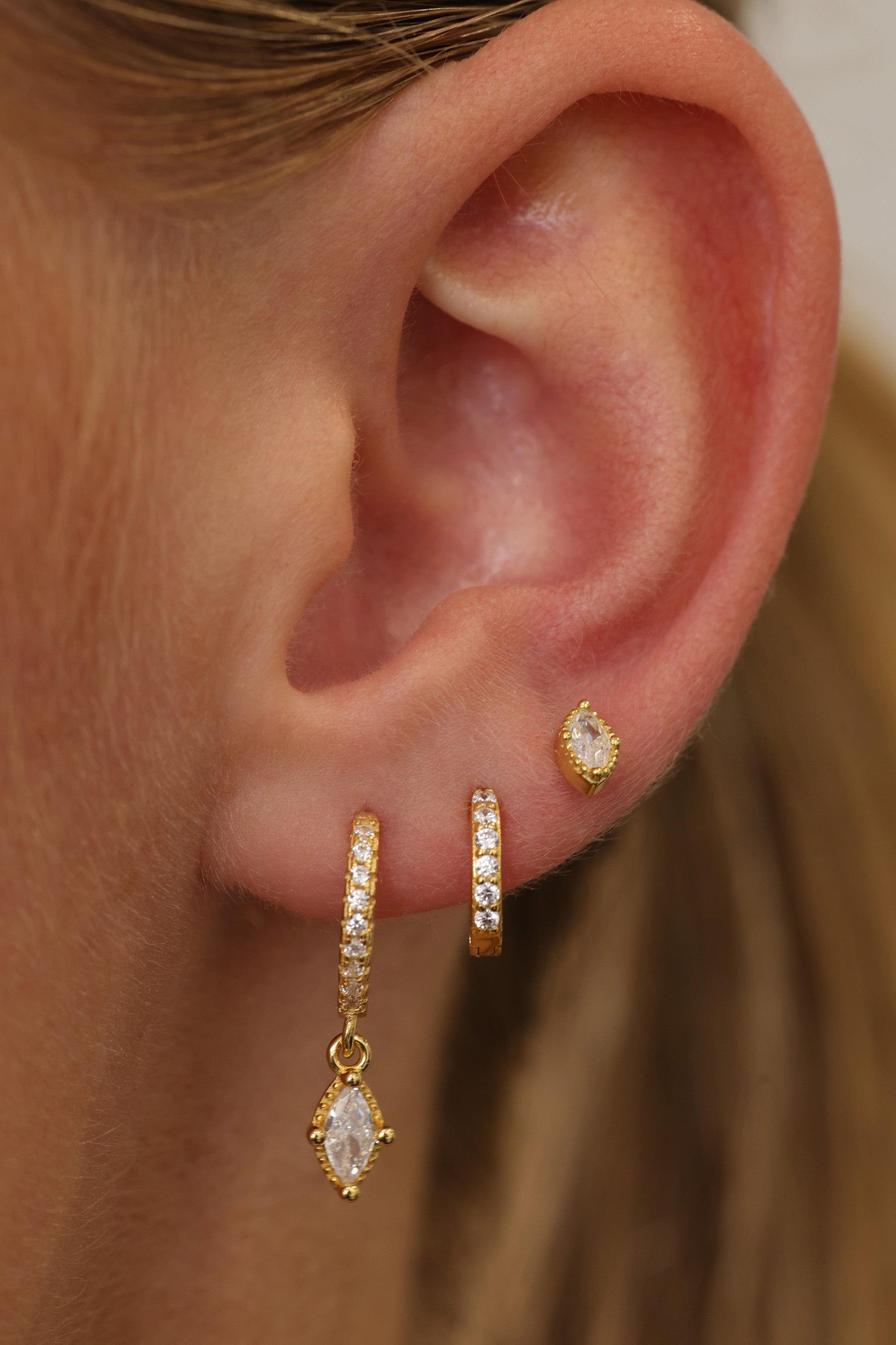 Sara gold three-piece ear stack worn on one ear — drop huggie, pave huggie and stud