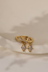 Pair of Sara gold marquise drop huggie earrings on a cream ceramic dish