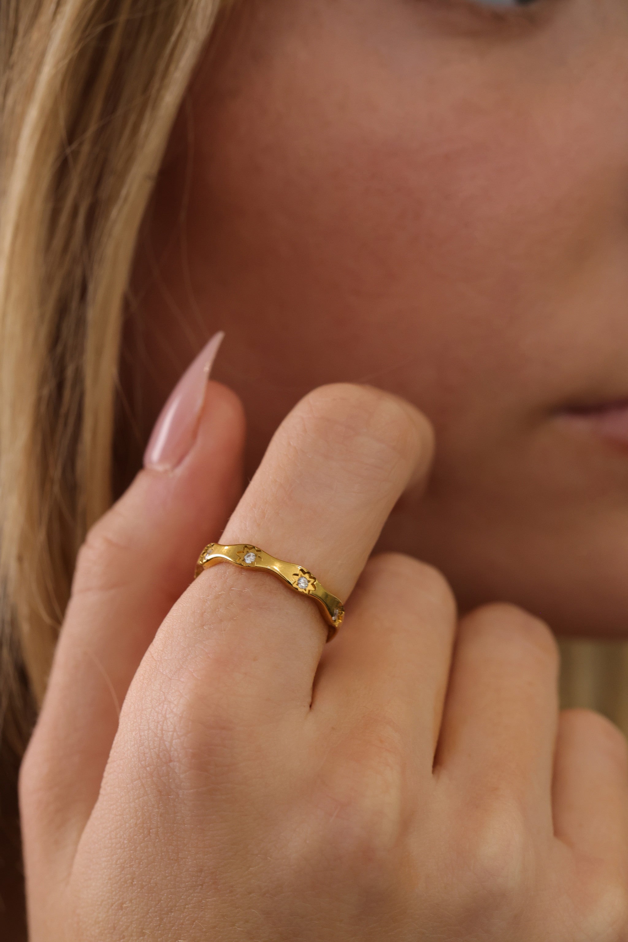 Delphine star eternity band in gold worn on a hand against white eyelet fabric