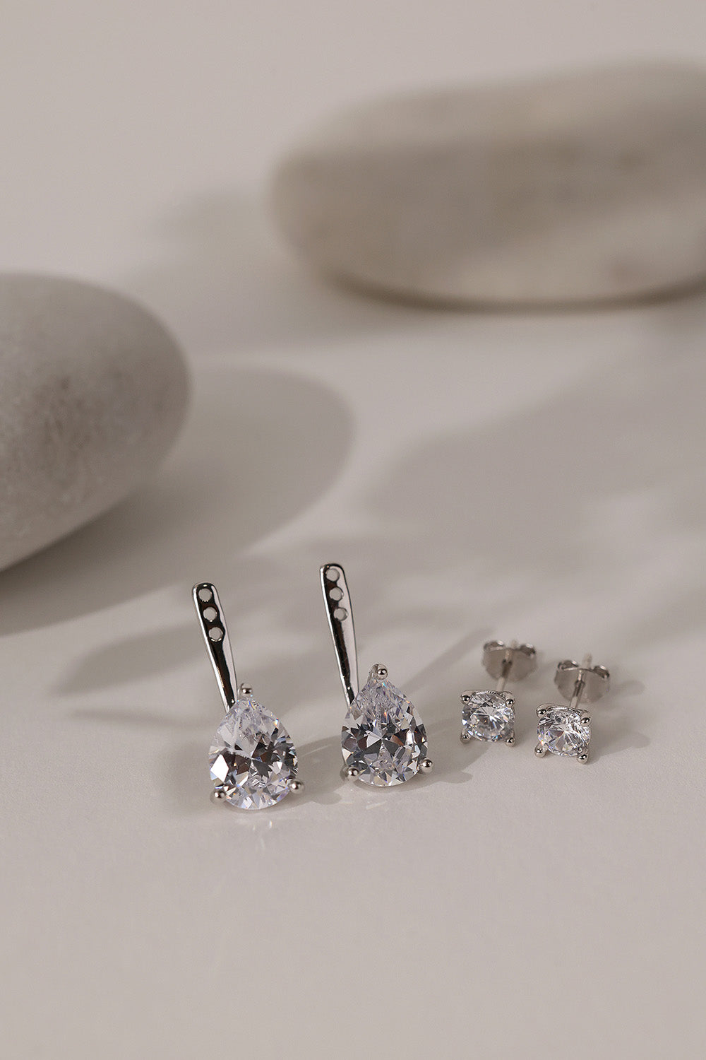Silver Adamas ear jackets showing the three adjustment holes, beside round studs and white pebbles.