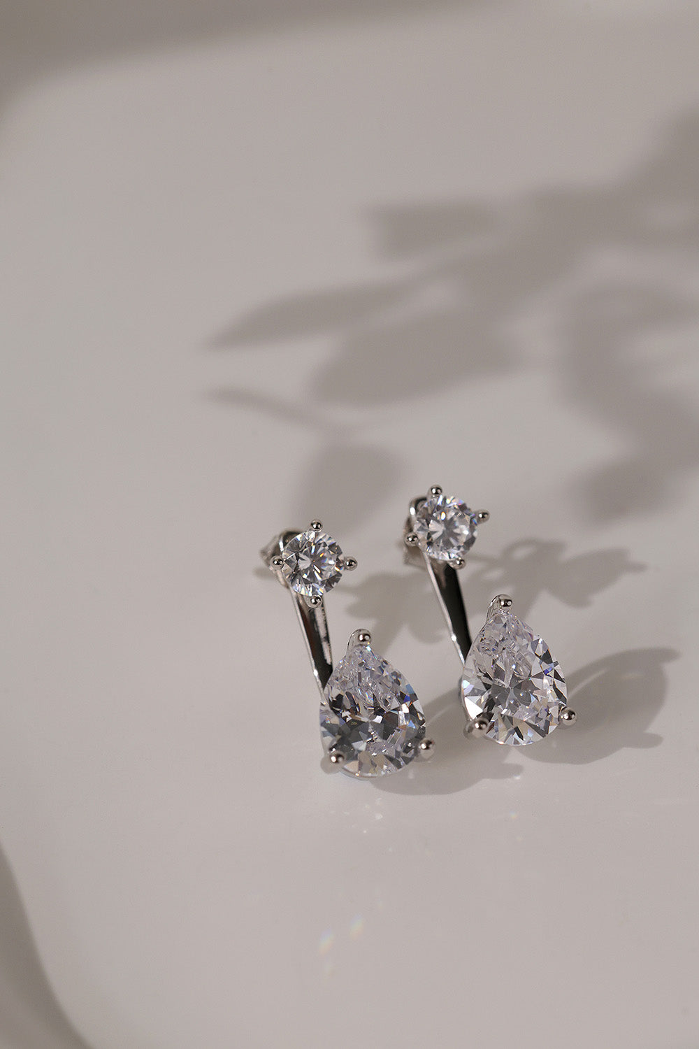 Pair of rhodium-plated Adamas ear jacket earrings lying flat on cream with soft shadows.