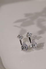 Pair of rhodium-plated Adamas ear jacket earrings lying flat on cream with soft shadows.