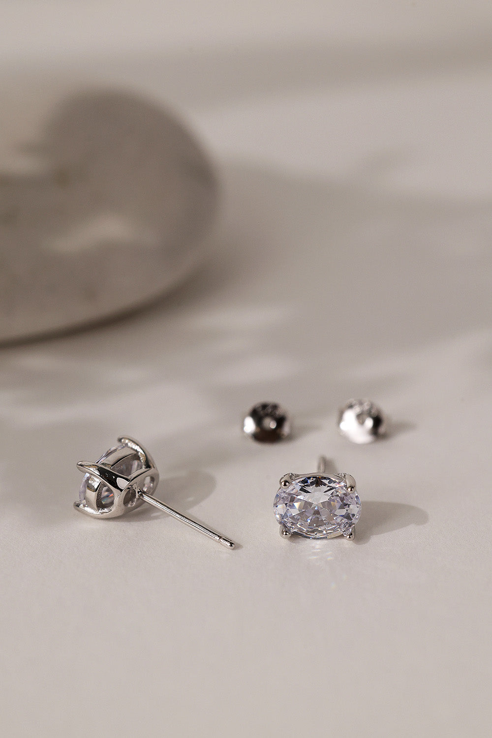 Pair of silver Adamas oval stud earrings lying on cream with their butterfly backs.