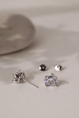 Pair of silver Adamas oval stud earrings lying on cream with their butterfly backs.