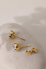Pair of gold Adamas oval stud earrings resting on a pale pebble with their butterfly backs.