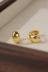 Gold Cleo huggie hoop earrings worn on the lobe — a chunky dome hoop in an ear stack.