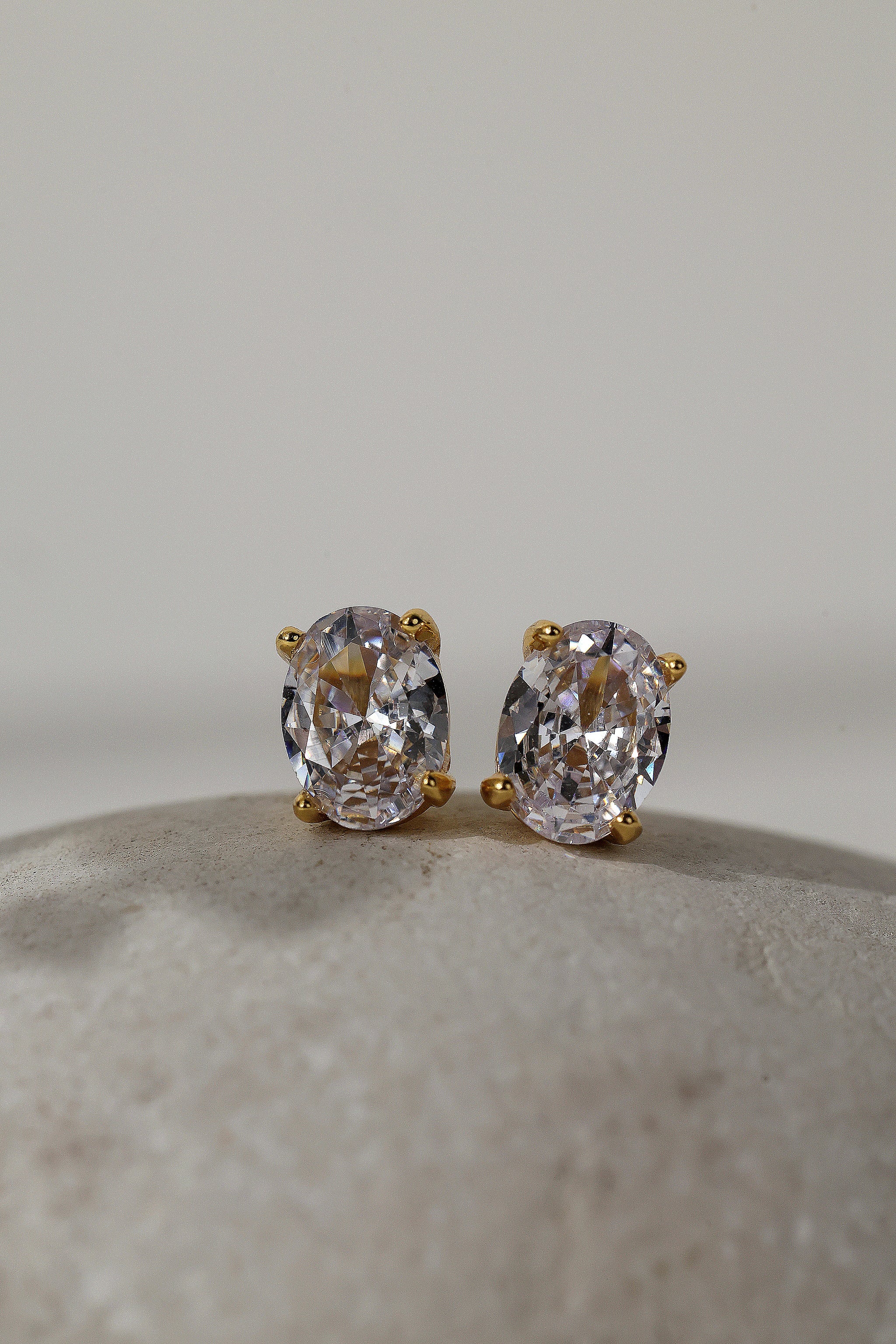 Close-up of gold oval cubic zirconia stud earrings, 8mm by 6mm stones in four-prong settings.