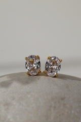 Close-up of gold oval cubic zirconia stud earrings, 8mm by 6mm stones in four-prong settings.