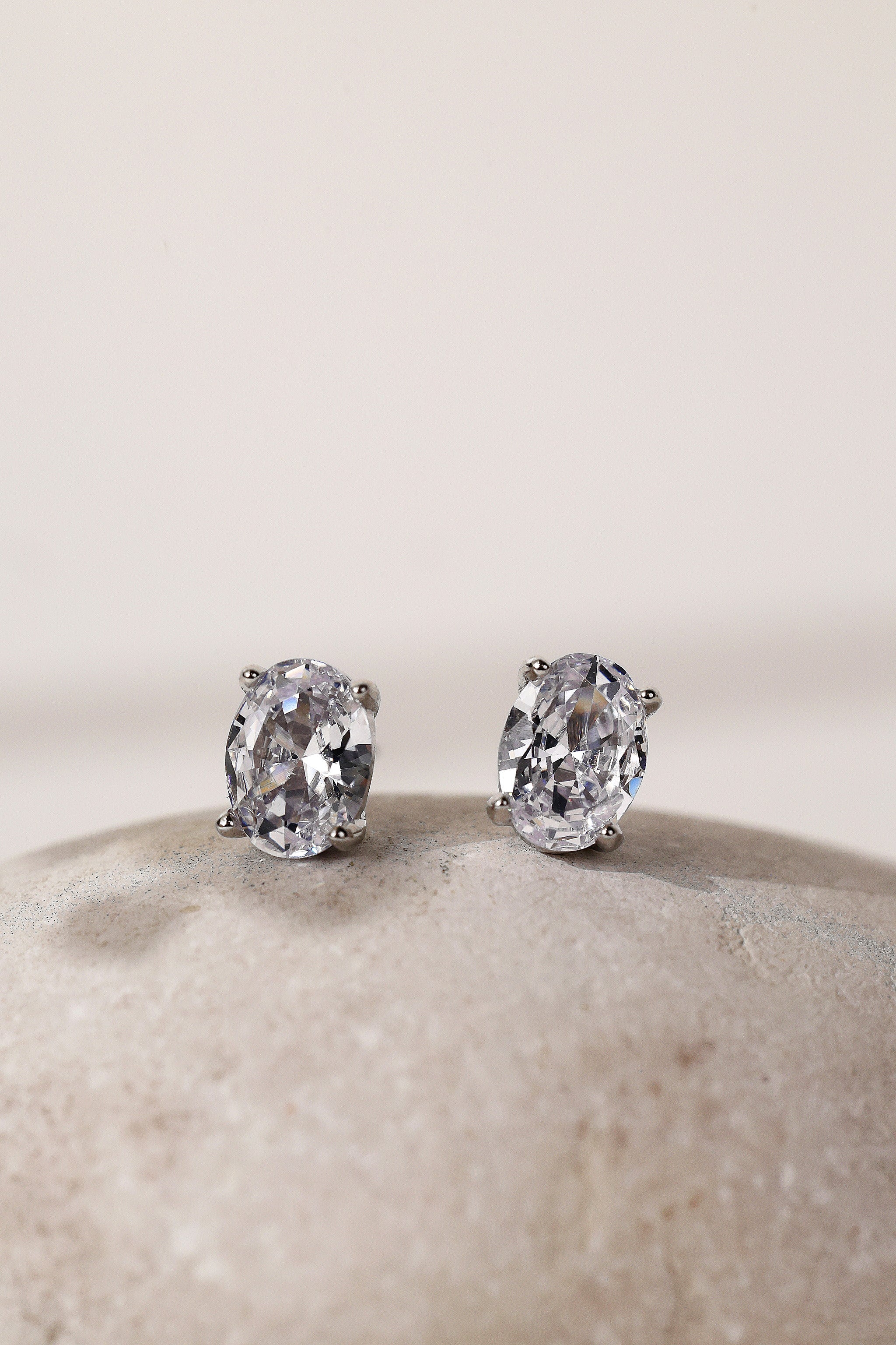 Close-up of silver oval cubic zirconia stud earrings, 8mm by 6mm stones on a pale stone.