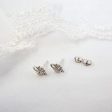 A pair of silver butterfly stud earrings with small clear rhinestones, displayed on a soft white textured surface with a white lace prop in the background.