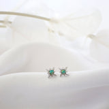 A pair of silver star-shaped stud earrings with round green opal  gemstones, resting on a soft white fabric surface.