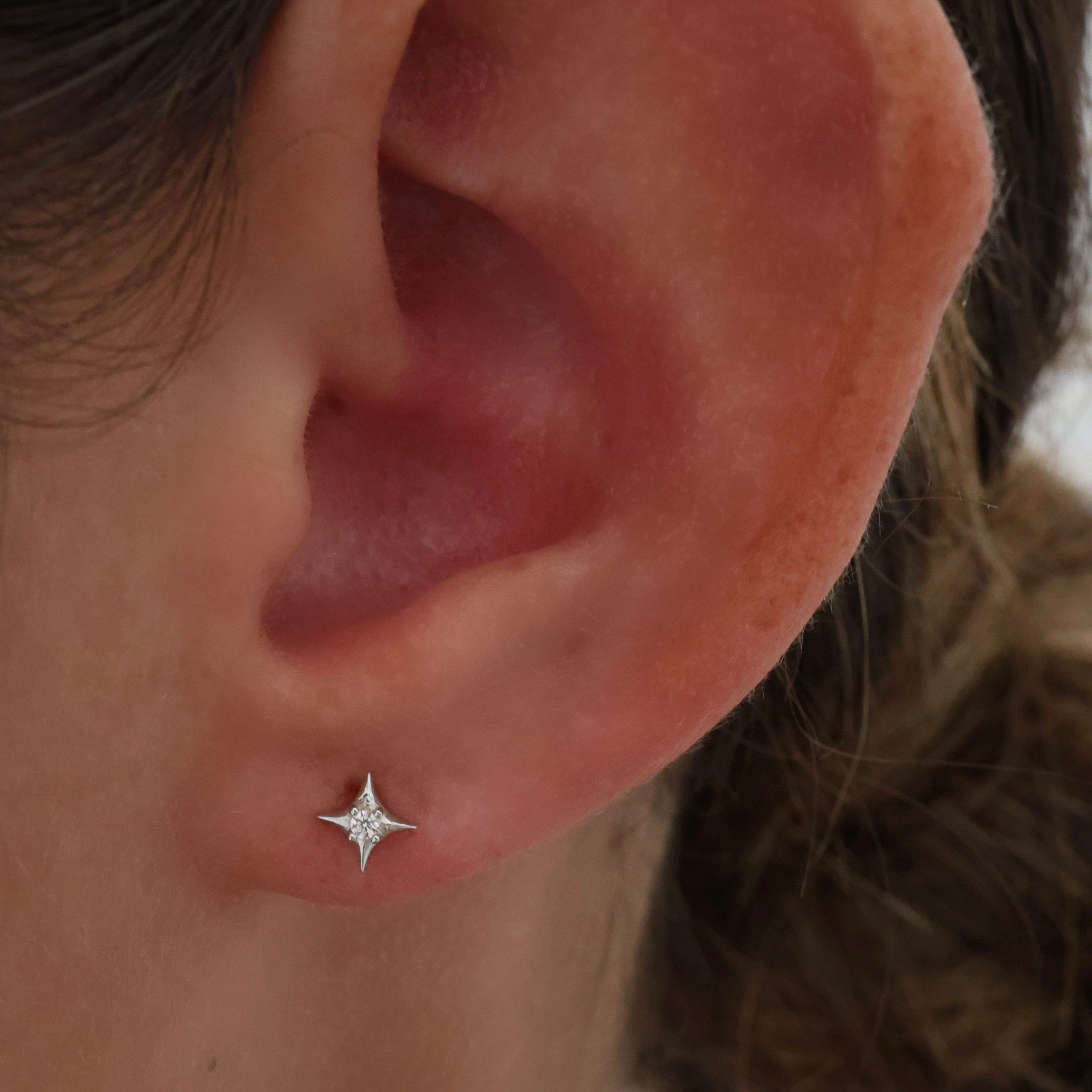 A close-up of a person's ear wearing a small silver star stud earring with tiny clear stones.