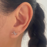 A close-up of a person's ear wearing a small silver bow-shaped stud earring.
