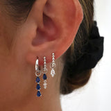 Close-up of an ear wearing silver earrings with blue and clear gemstones.