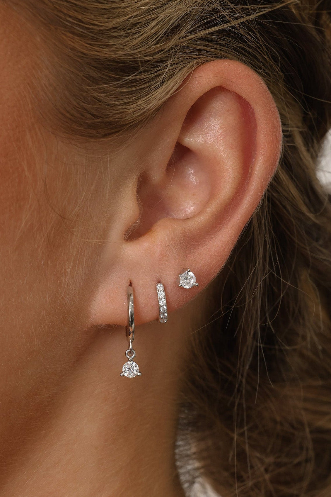 A three‑pair sterling silver earring set featuring a CZ dangle earring, a small cubic zirconia huggie hoop, and a delicate CZ stud. All pieces are rhodium‑plated 925 sterling silver, hypoallergenic, nickel‑free, and displayed together as a coordinated trio.