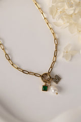 Gold stainless steel necklace with pearl, green birthstone charm, and crystal initial charm on an easy‑open hook.