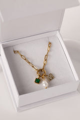 Gold stainless steel necklace with pearl, green birthstone charm, and crystal initial charm on an easy‑open hook.
