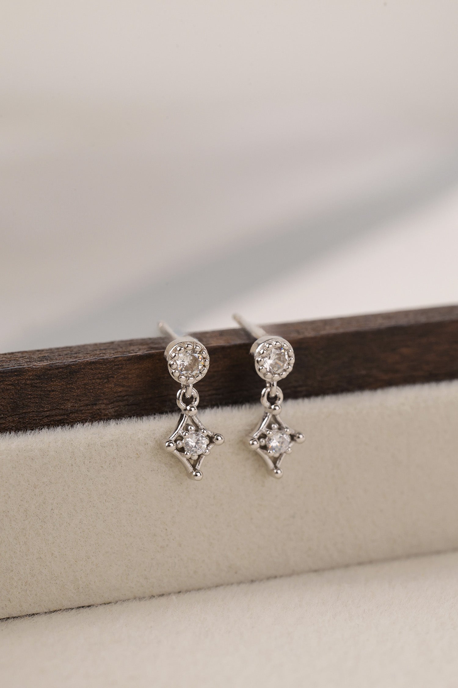 Silver earrings with star-shaped drops on a wooden stand.