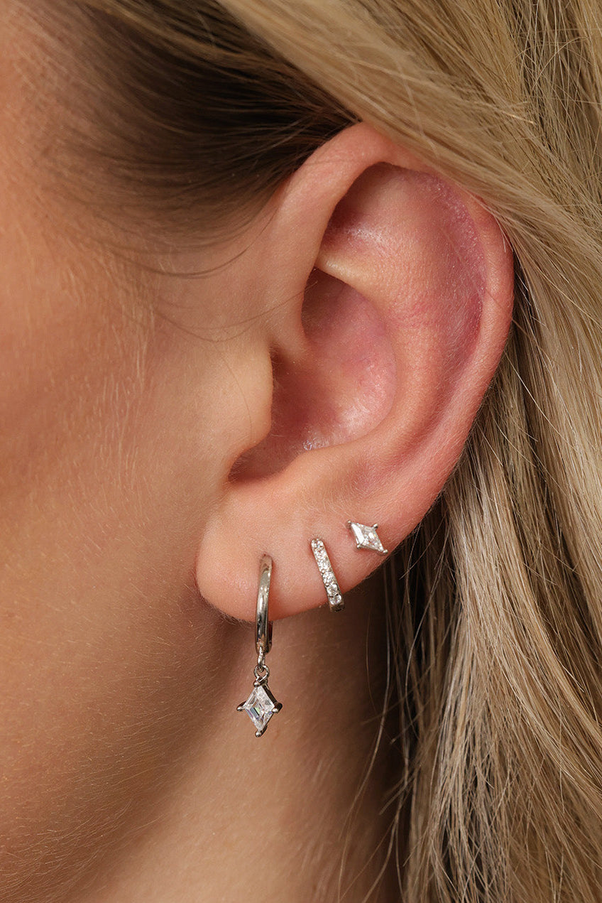 A sterling silver three‑piece earring set featuring a CZ dangle earring, a small CZ huggie, and a delicate teardrop‑shaped stud. Each piece is rhodium‑plated 925 sterling silver with brilliant AAAAA cubic zirconia, designed for a sparkling, elegant look.
