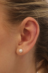 Small freshwater pearl stud earring worn on the earlobe, shown in a gold stainless steel setting.