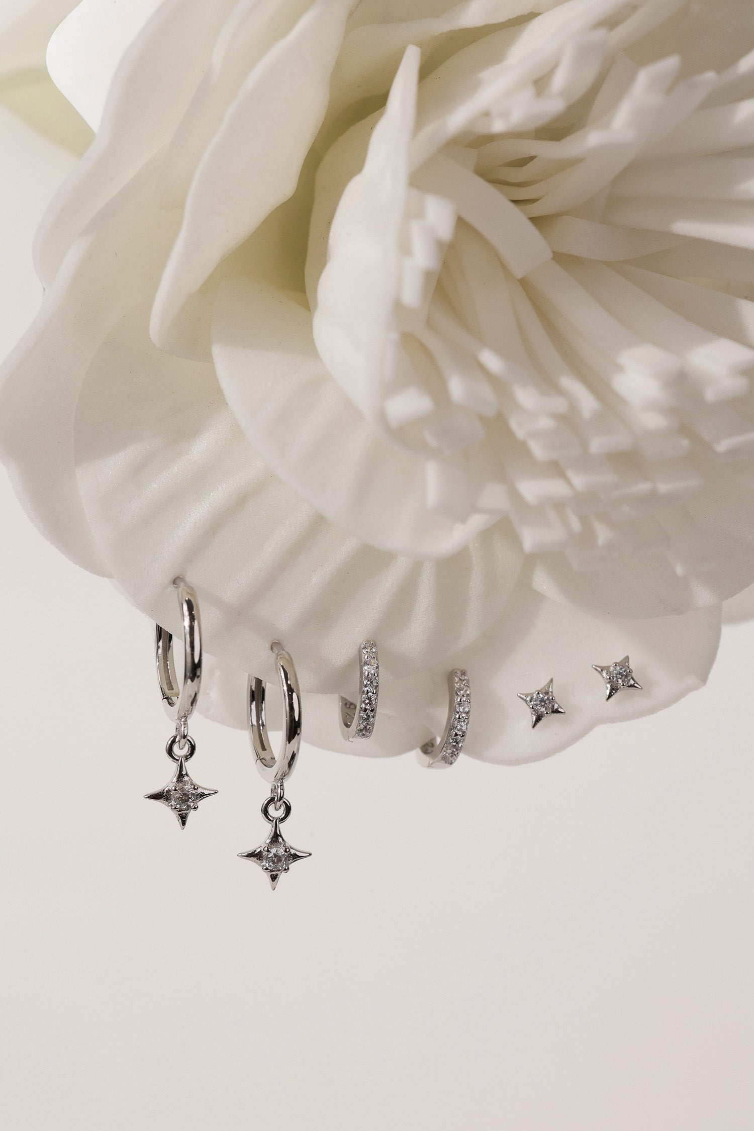 A three‑pair celestial silver earring set featuring a star stud, a moon‑shaped huggie, and a sparkling dangle charm, displayed together for an elegant, versatile look.