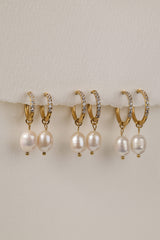 Three sizes of gold pavé waterproof hoop earrings with natural freshwater pearl drops displayed on a textured neutral background
