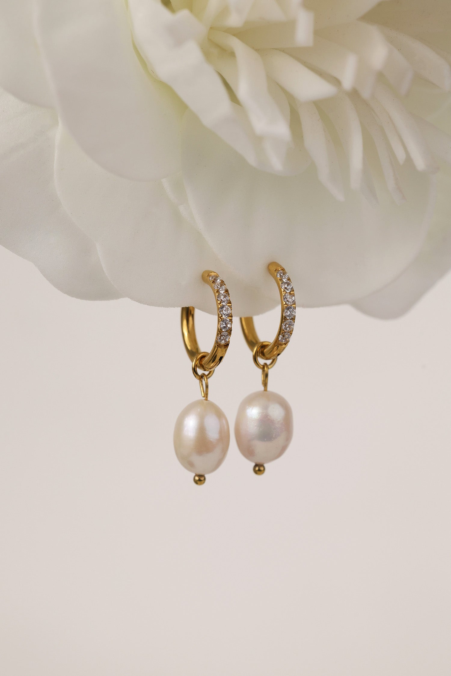 Three sizes of gold pavé waterproof hoop earrings with natural freshwater pearl drops displayed on a textured neutral background