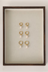 Three sizes of gold pavé waterproof hoop earrings with natural freshwater pearl drops displayed on a textured neutral background
