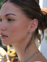 White gold‑plated hoop earrings with a 4mm baguette‑cut CZ dangle charm, shown in clear white, emerald green and pink