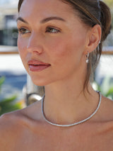 White gold‑plated hoop earrings with a 4mm baguette‑cut CZ dangle charm, shown in clear white, emerald green and pink