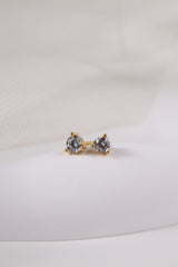 Pair of small gold round cubic zirconia stud earrings resting on cream fabric.