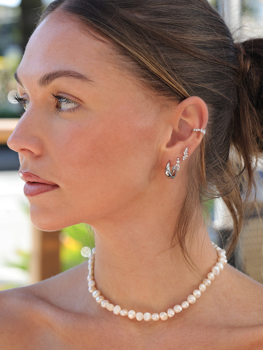 Woman wearing a pearl necklace and silver earrings with a blurred outdoor background