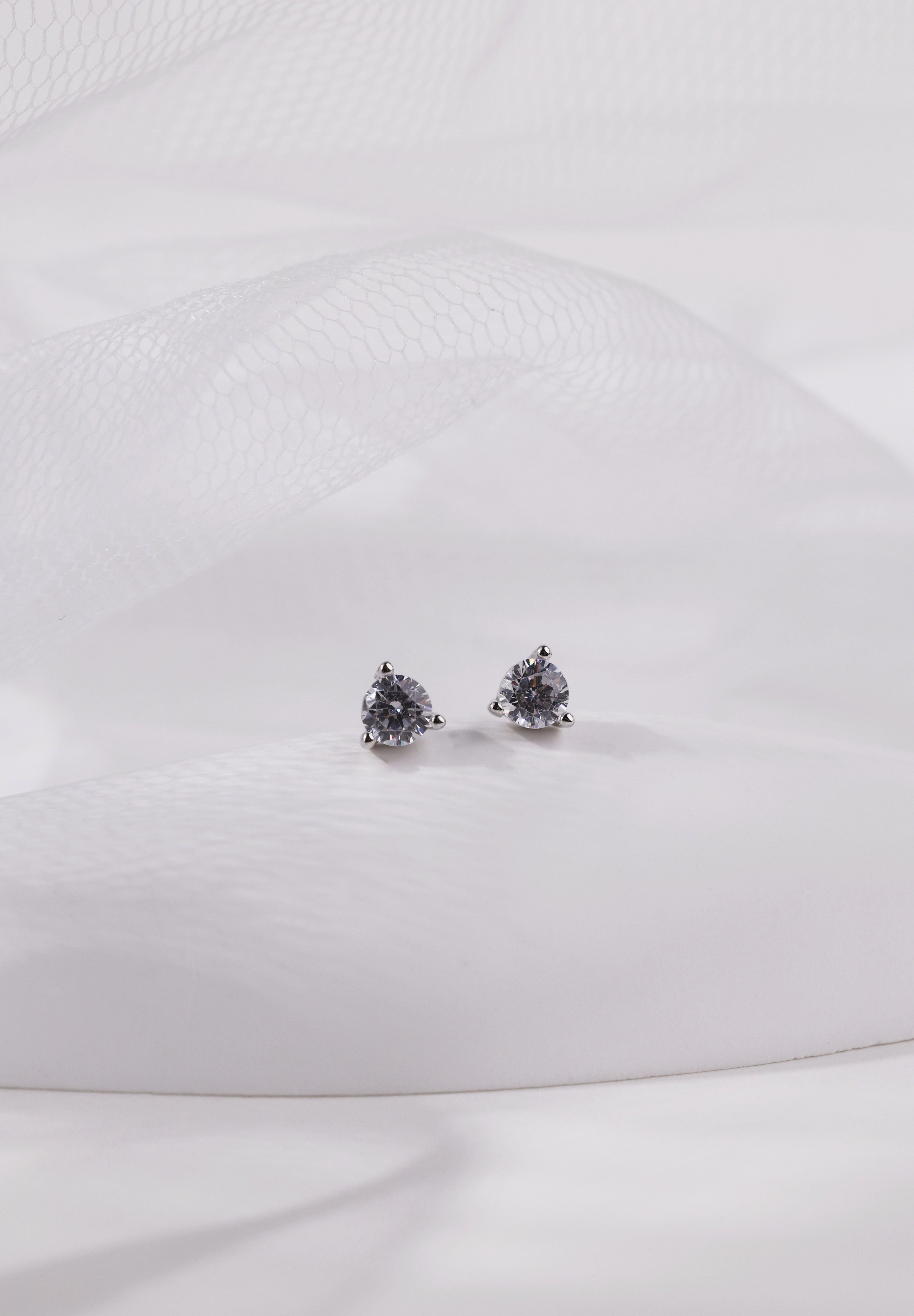 Pair of small silver round cubic zirconia stud earrings resting on white tulle.