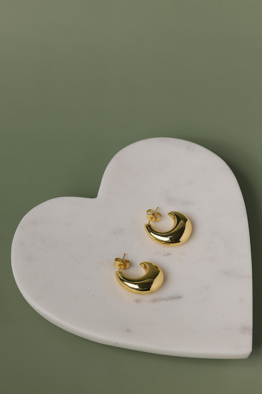 Gold hoop earrings on a heart-shaped marble stand against a green background
