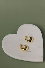 Gold hoop earrings on a heart-shaped marble stand against a green background