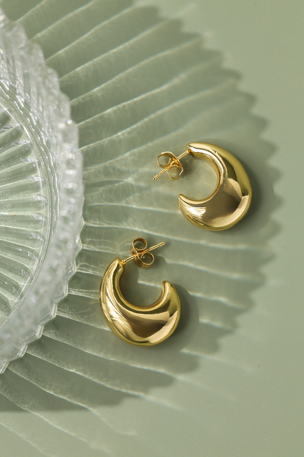 Gold hoop earrings on a textured green surface