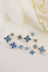 A set of small blue floral 4 clover stud earrings with gold-tone settings, arranged on soft white flower petals.