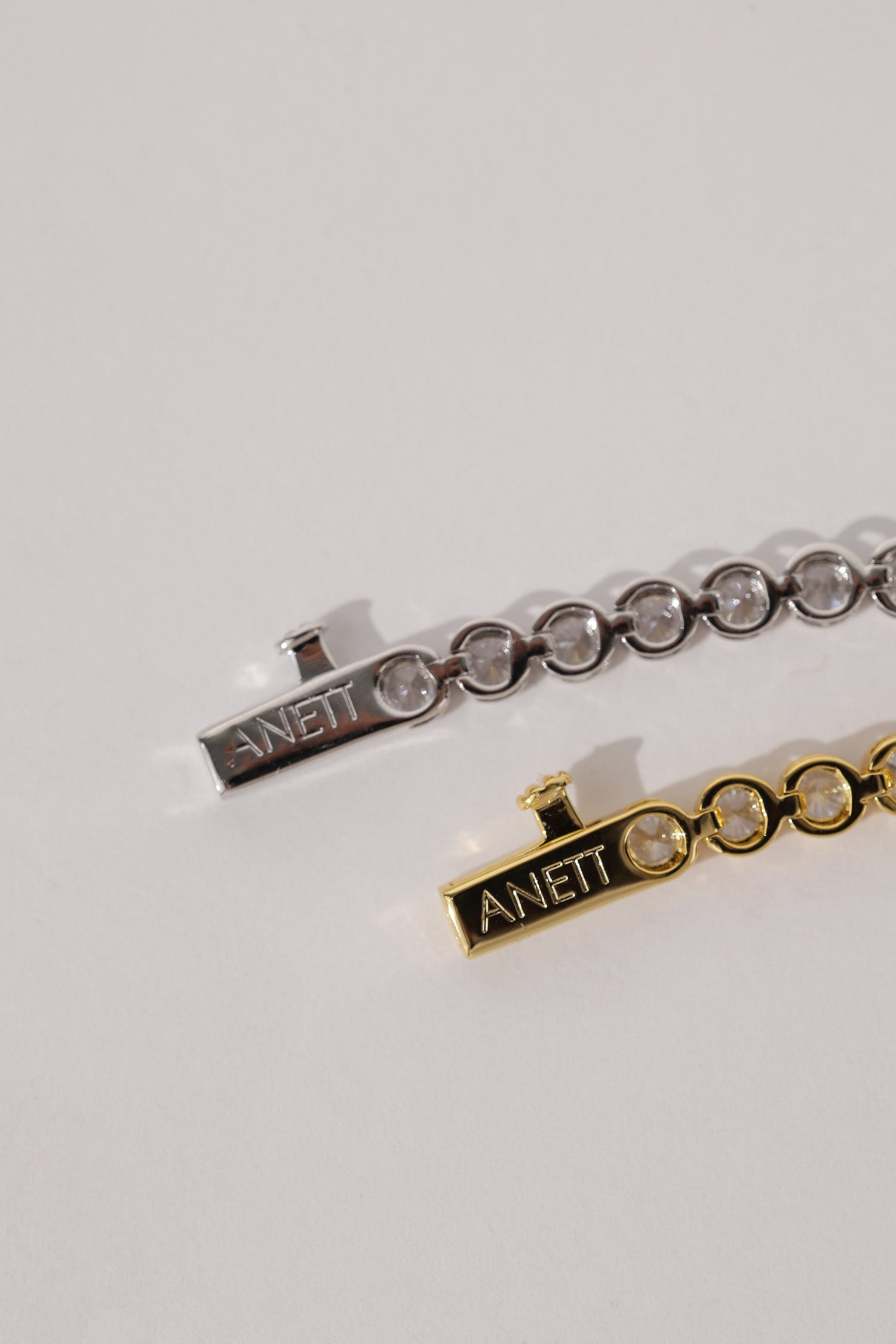Close-up of the silver bracelet clasp engraved with the ANETT brand name, alongside the gold version.