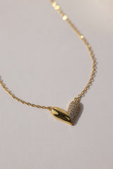 Elegant heart-shaped necklace in 18K gold-plated sterling silver with half pavé crystal detailing, displayed against a neutral background. Hypoallergenic and tarnish-resistant design.