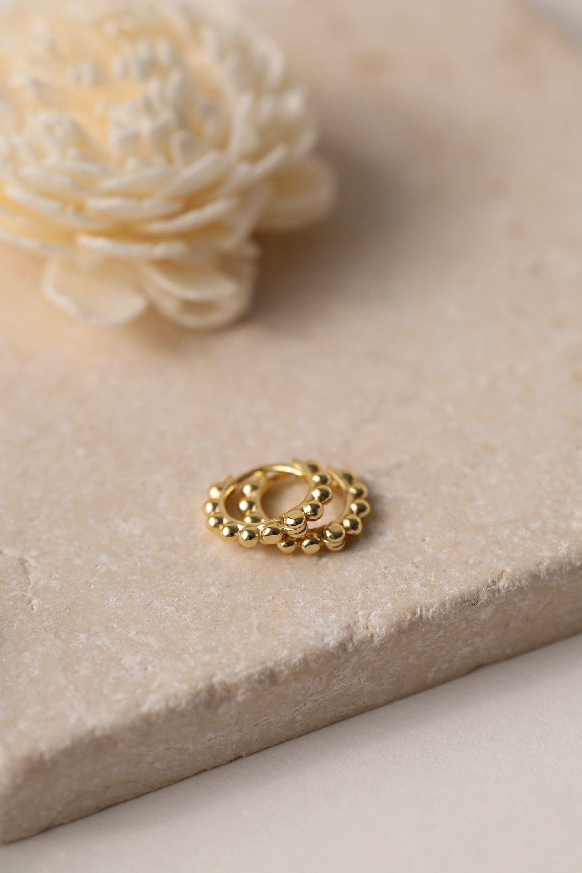 Sterling silver beaded hoop earrings in 8mm and 9mm sizes, featuring polished spherical detailing for a dainty, minimalist look. Displayed on a neutral textured surface with soft floral accents.