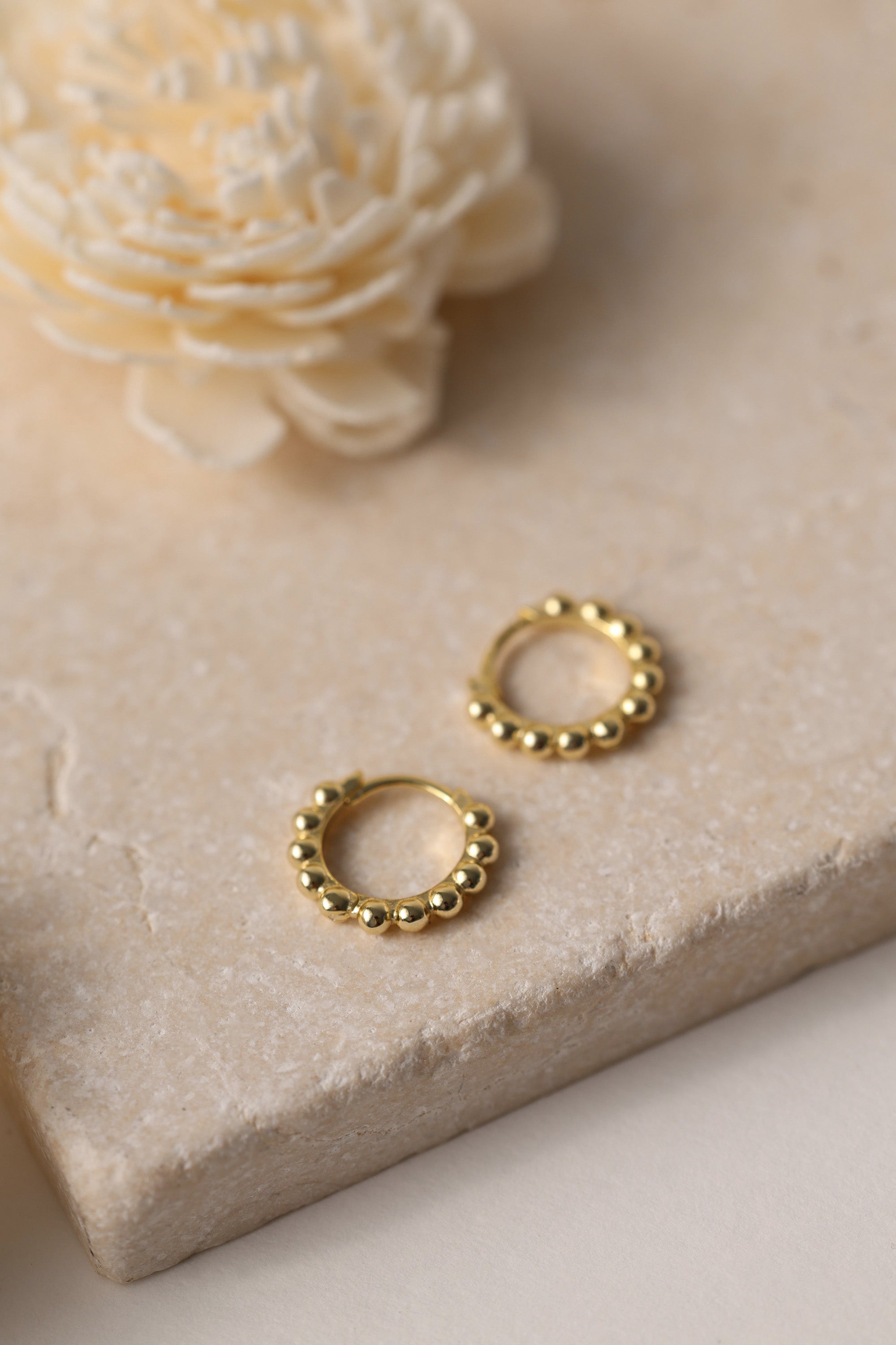 Sterling silver beaded hoop earrings in 8mm and 9mm sizes, featuring polished spherical detailing for a dainty, minimalist look. Displayed on a neutral textured surface with soft floral accents.