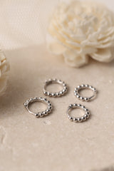 Sterling silver beaded hoop earrings in 8mm and 9mm sizes, featuring polished spherical detailing for a dainty, minimalist look. Displayed on a neutral textured surface with soft floral accents.