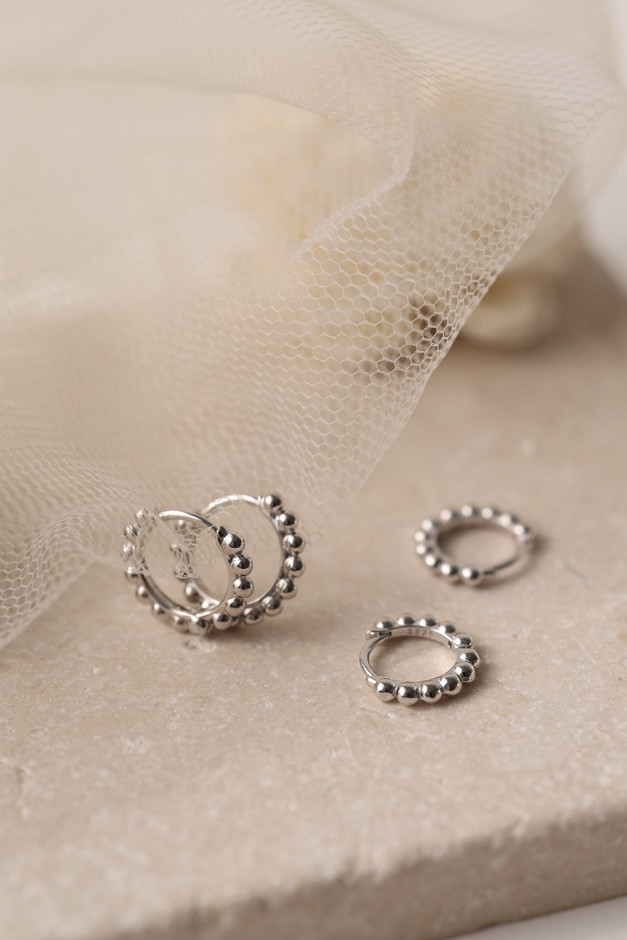 Sterling silver beaded hoop earrings in 8mm and 9mm sizes, featuring polished spherical detailing for a dainty, minimalist look. Displayed on a neutral textured surface with soft floral accents.