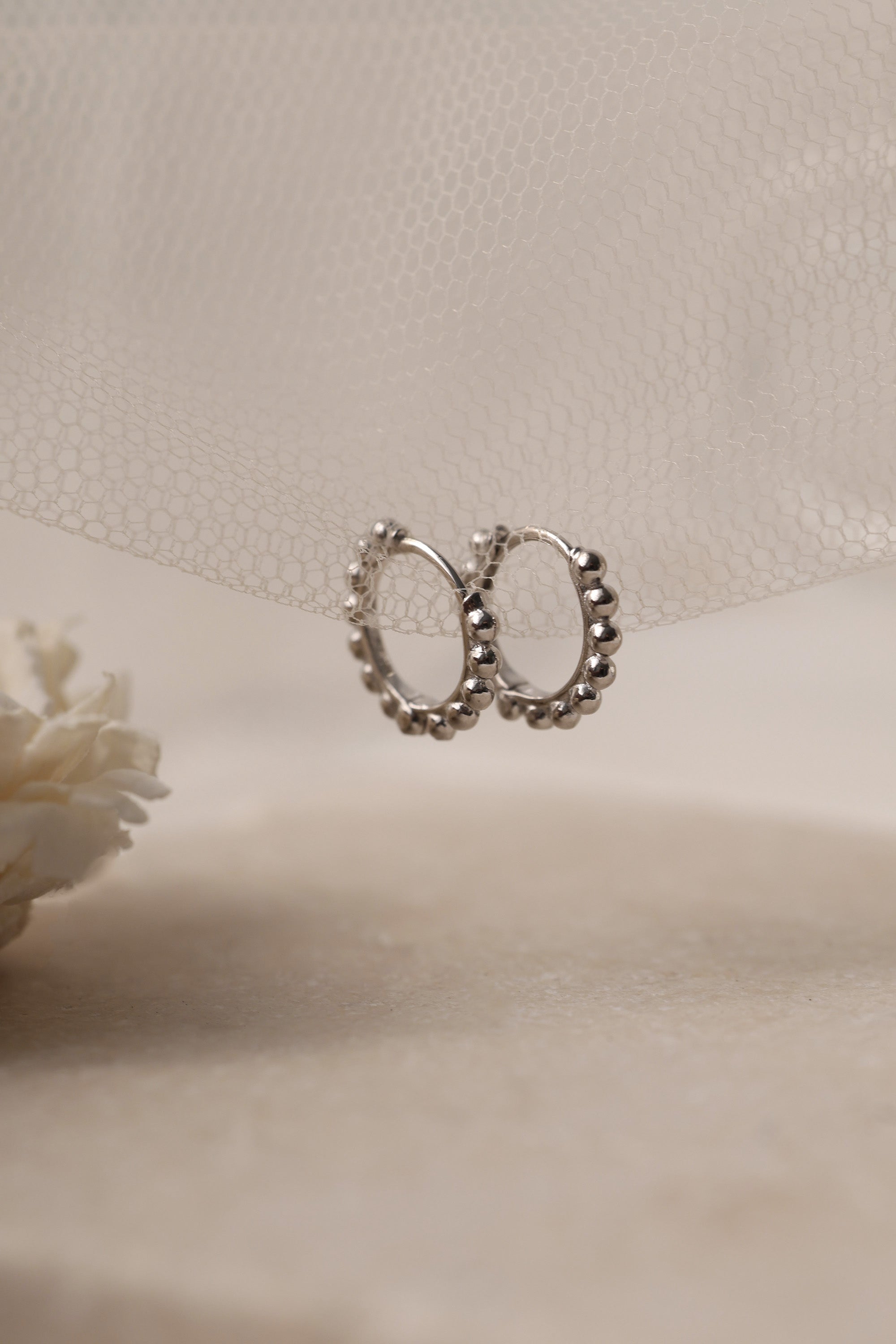 Sterling silver beaded hoop earrings in 8mm and 9mm sizes, featuring polished spherical detailing for a dainty, minimalist look. Displayed on a neutral textured surface with soft floral accents.