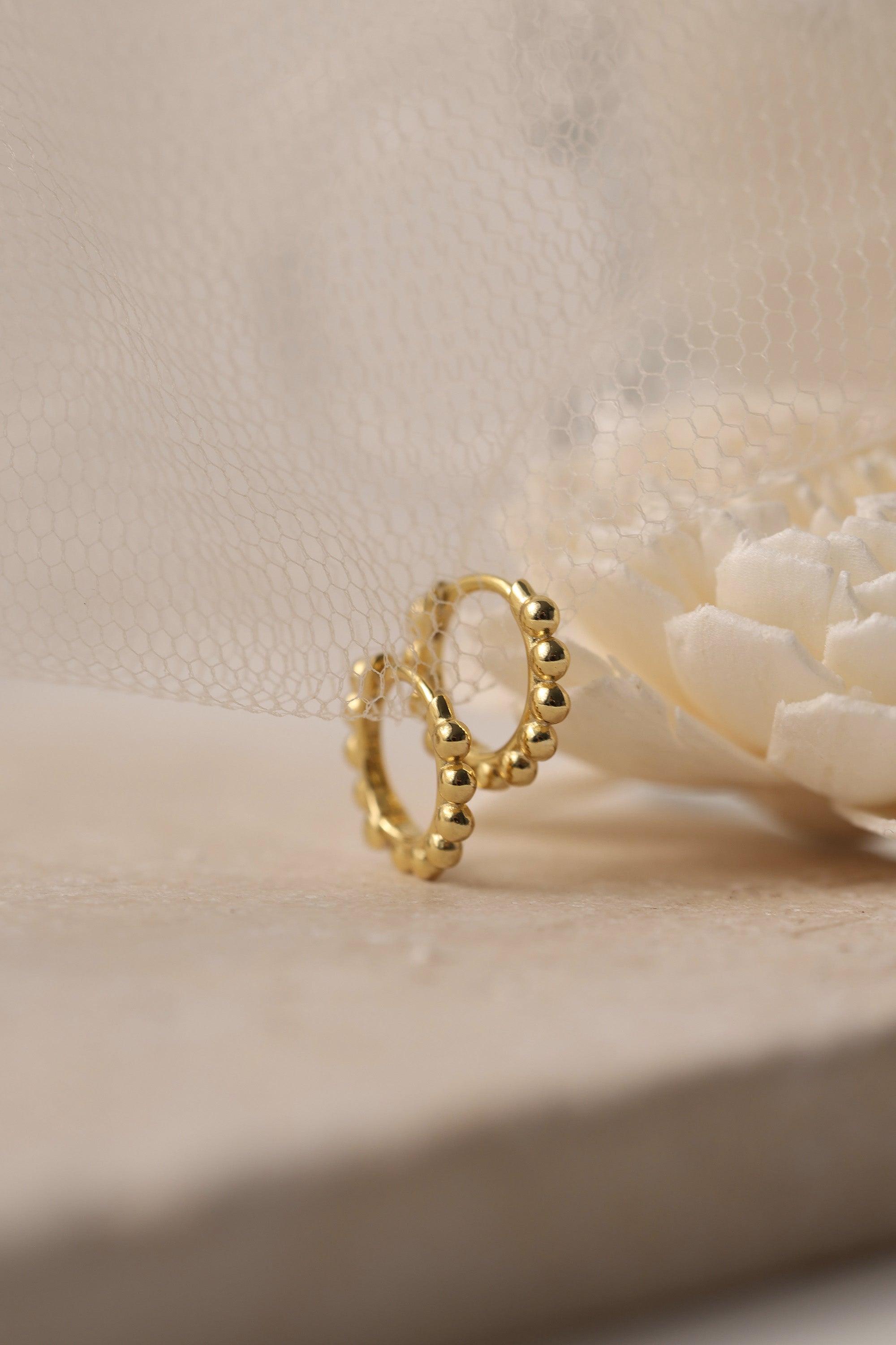 Sterling silver beaded hoop earrings in 8mm and 9mm sizes, featuring polished spherical detailing for a dainty, minimalist look. Displayed on a neutral textured surface with soft floral accents.