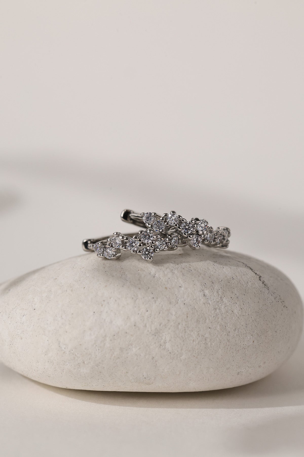 A silver-toned ring with a cluster of clear pavé stones, displayed on a smooth white stone against a warm off-white background.