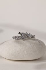 A silver-toned ring with a cluster of clear pavé stones, displayed on a smooth white stone against a warm off-white background.